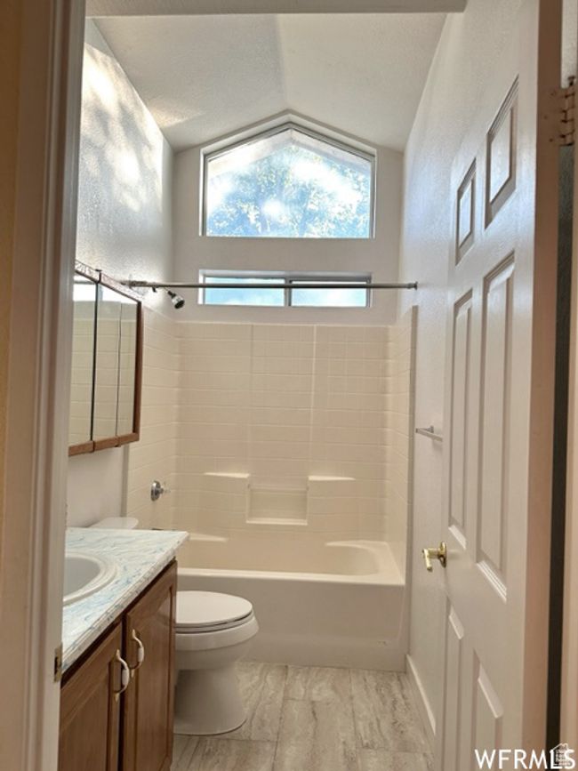 Bathroom featuring a textured ceiling, toilet, vanity, lofted ceiling, and shower / bathing tub combination | Image 44