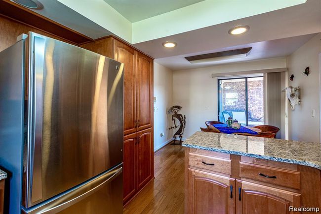 Kitchen featuring freestanding refrigerator, recessed lighting, light stone countertops, light wood-style floors, and brown cabinetry | Image 6