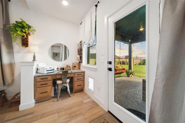 This cozy home office features a built-in desk with ample storage and a stylish metal chair. A glass door opens to a covered patio overlooking a spacious backyard, offering plenty of natural light and a seamless indoor-outdoor connection. | Image 25