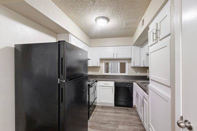 Kitchen with dark countertops, black appliances, light wood-style flooring, white cabinets, and a textured ceiling | Image 25