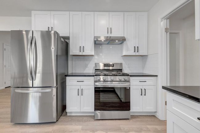 Kitchen featuring appliances with stainless steel finishes, under cabinet range hood, white cabinets, light wood-style floors, and dark countertops | Image 9