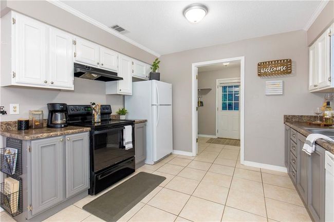 Kitchen featuring black range with electric stovetop, under cabinet range hood, freestanding refrigerator, dark countertops, and ornamental molding | Image 9