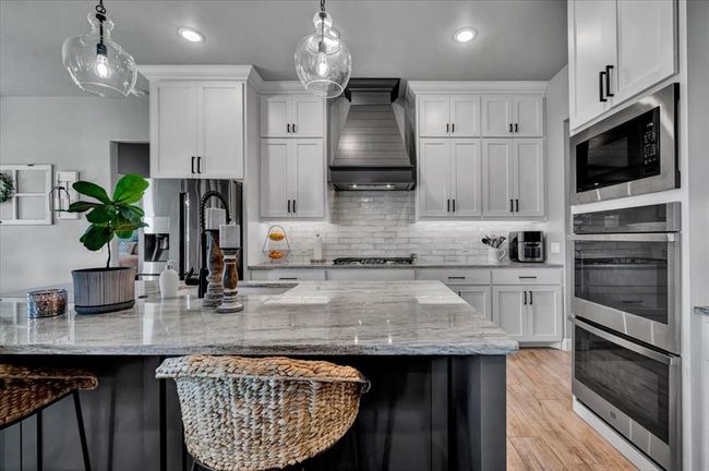 Kitchen with custom exhaust hood, appliances with stainless steel finishes, white cabinets, a breakfast bar, and recessed lighting | Image 19