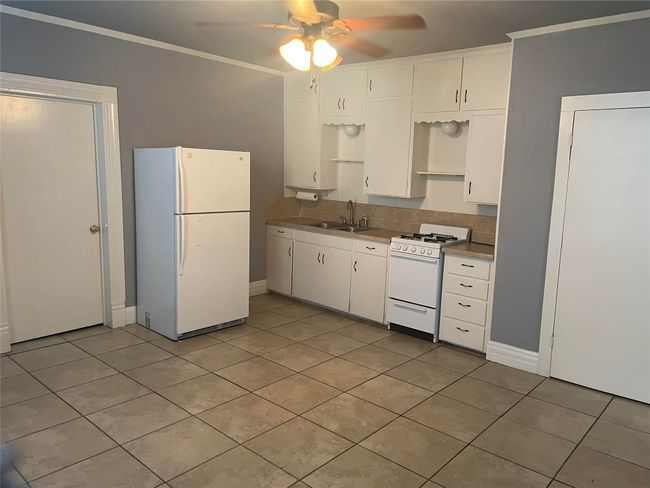 Kitchen featuring white appliances, ceiling fan, light tile patterned flooring, white cabinetry, and crown molding | Image 8