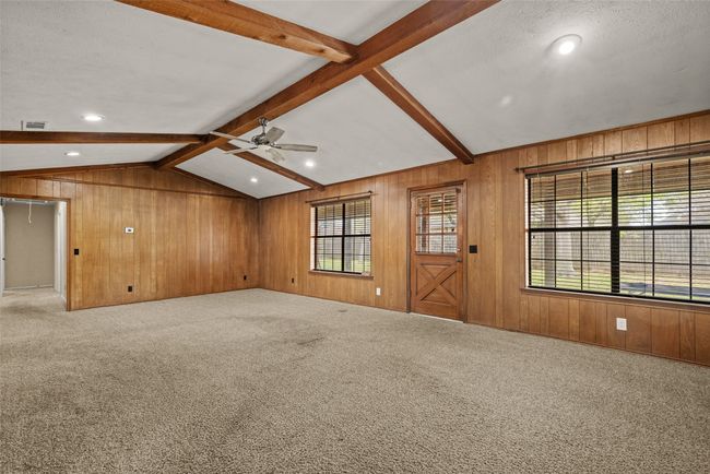 Unfurnished living room with lofted ceiling with beams, carpet floors, ceiling fan, and wooden walls | Image 9