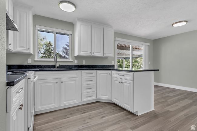 Kitchen with light wood finished floors, a sink, range, a peninsula, and white cabinetry | Image 14