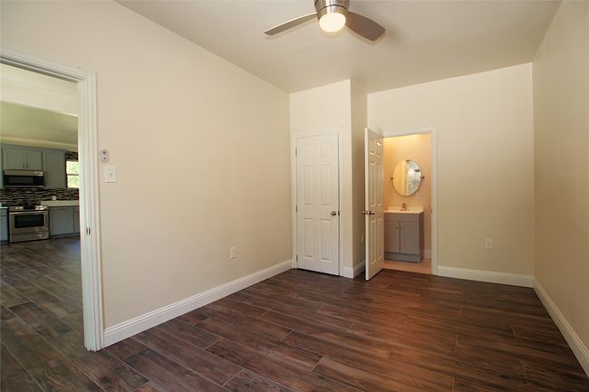 Unfurnished bedroom with dark wood-type flooring, baseboards, connected bathroom, and a ceiling fan | Image 5