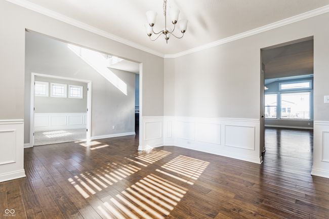 unfurnished dining area with hardwood / wood-style floors, a decorative wall, crown molding, wainscoting, and a chandelier | Image 7