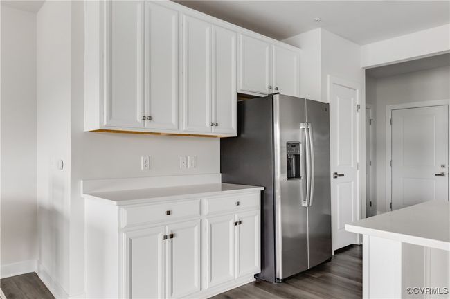 Kitchen with stainless steel fridge with ice dispenser, dark wood finished floors, white cabinetry, and light countertops | Image 13