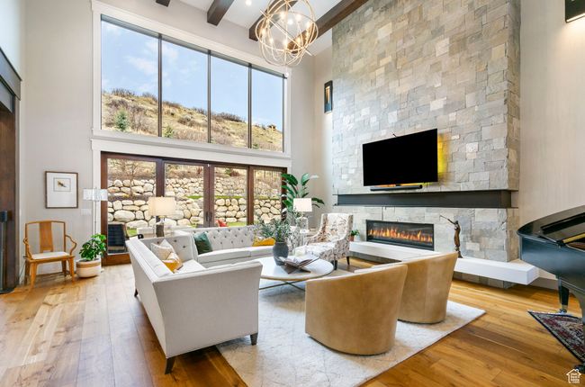 Living area featuring a stone fireplace, an inviting chandelier, a high ceiling, beamed ceiling, and hardwood / wood-style floors | Image 20