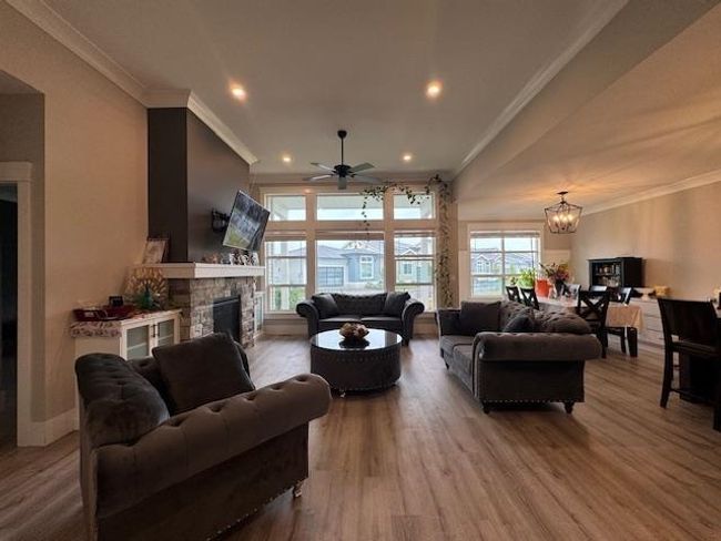 Living room with a stone fireplace, wood finished floors, ornamental molding, and ceiling fan with notable chandelier | Image 19